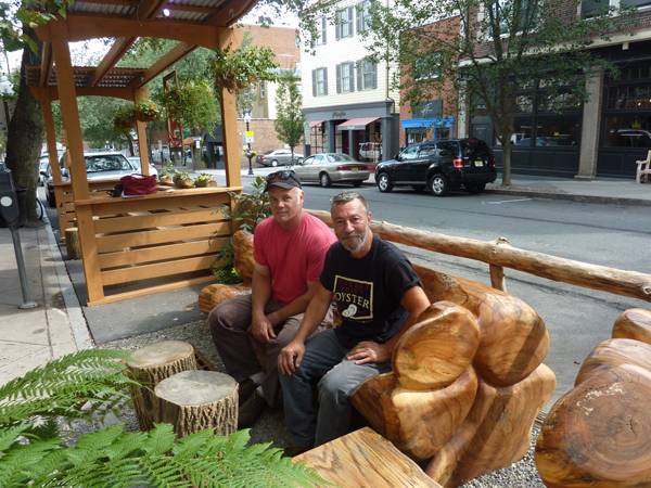 CREATIVITY AT REST: Landscape artist and ideas man Peter Soderman (left) and wood and metal artist Greg Napolitan take time out to enjoy Princeton’s first Parklet in front of Small World Coffee on Witherspoon Street. Mr. Napolitan carved the two huge wooden benches in the parklet after being contacted by Mr. Soderman to participate in the tiny park that takes up two parking spots in front of the coffee shop. The project was a the result of a joint effort by the municipality, the Arts Council of Princeton, and several members of Princeton’s creative community.(Photo by L. Arntzenius)